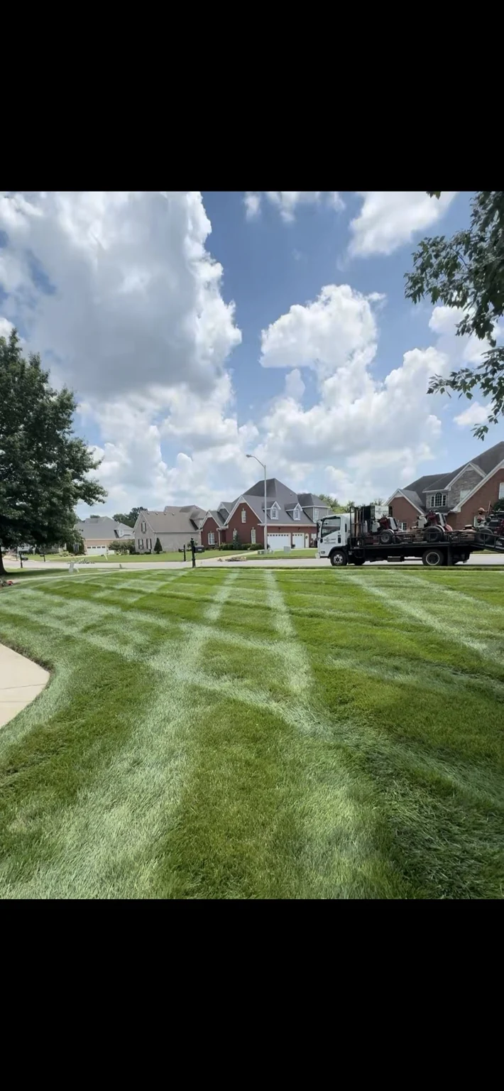 Striped front lawn with a landscaping truck and mowers nearby